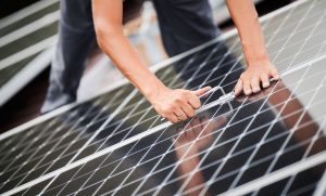 A professional solar technician installs a solar panel onto a property roof