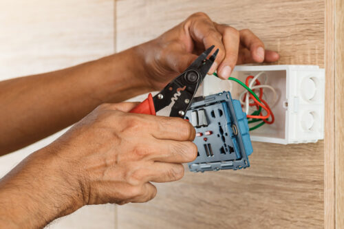 an electrician uses a wire stripper while installing an outlet